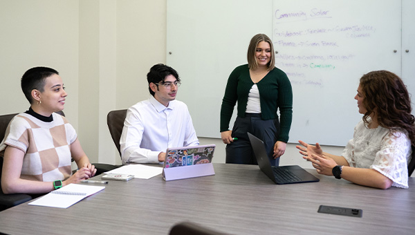 Maddie Curtis, Edgardo Diaz Velazquez, Hanna Theile, and Belen Torres work together with a white board in the background.