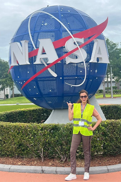 Khadija Taki stands in front of a blue globe with the NASA logo on it.