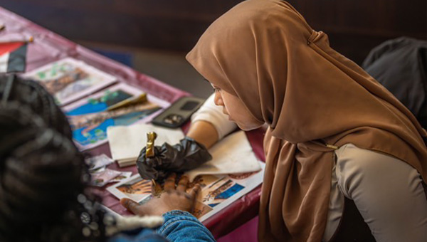 Samiha paints a henna design on someone's hand.